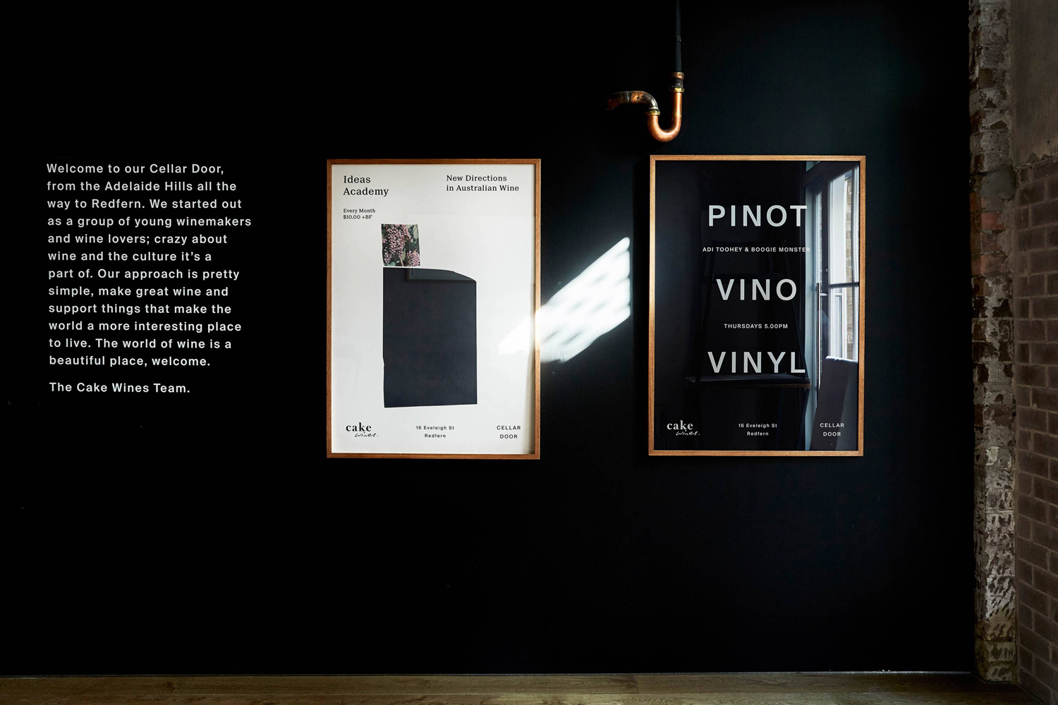 Two framed posters mounted on a black wall with descriptive text and graphic design elements for Cake Wines.