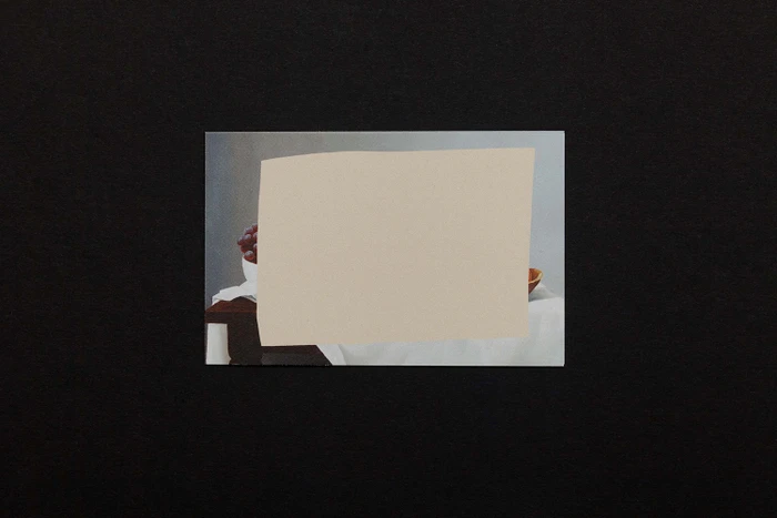 Still life painting print partially covered by a beige paper cutout, set against a black background.