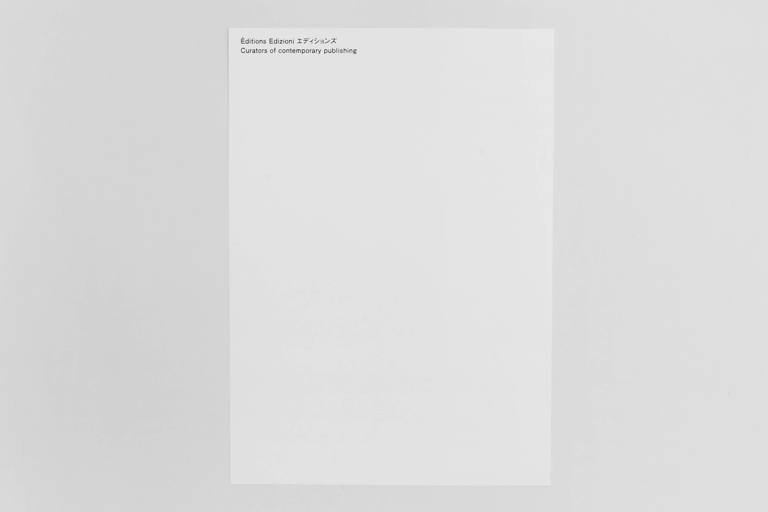 Minimalist white paper sheet featuring typography in the top left corner resting on a plain neutral grey surface.