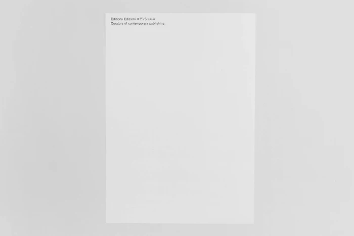 Minimalist white paper sheet featuring typography in the top left corner resting on a plain neutral grey surface.