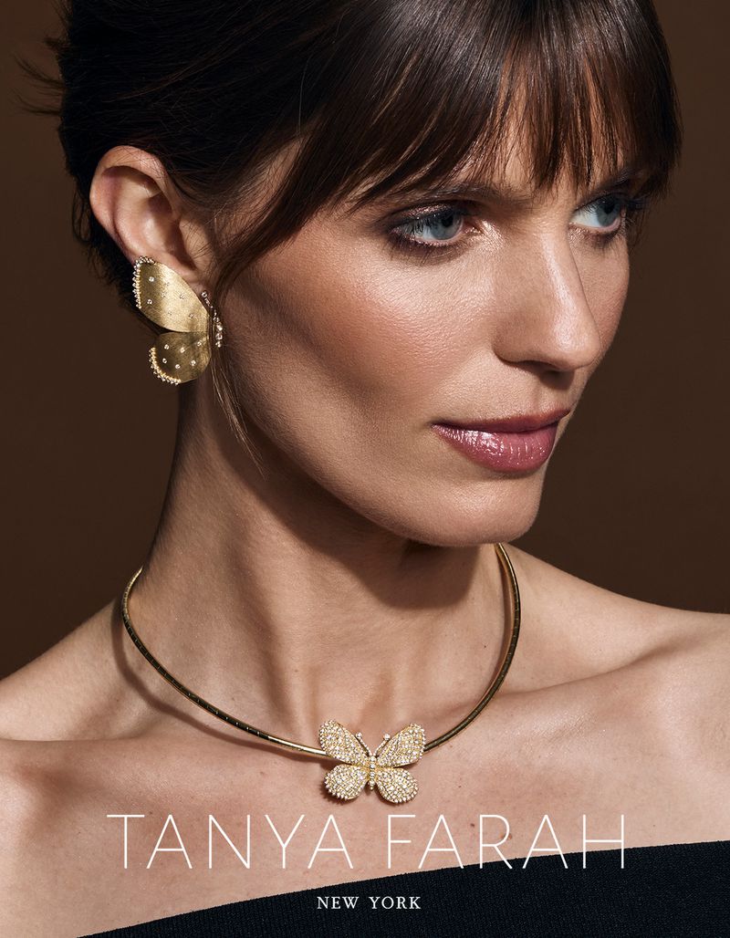 Close-up shot of a woman wearing gold butterfly-shaped earrings and necklace, showcasing fine jewelry against a brown background.
