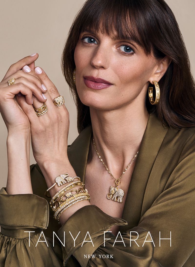 Close-up of an adult female jewelry model showcasing gold rings, hoop earrings, bracelets, and a necklace with elephant charms.