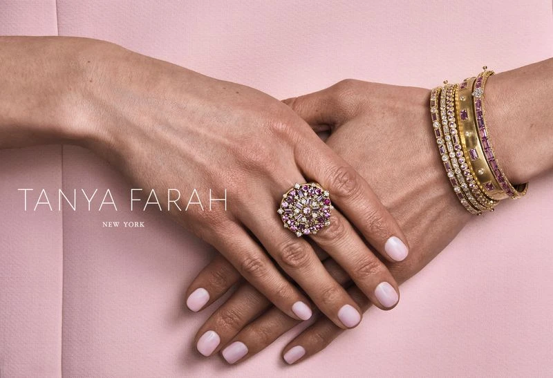Close-up shot of woman's hands adorned with a cocktail ring and bracelets. Soft pink background creates a delicate, fashion-forward aesthetic.
