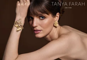Model wearing gold butterfly earrings and a matching statement cuff bracelet by Tanya Farah against a dark background