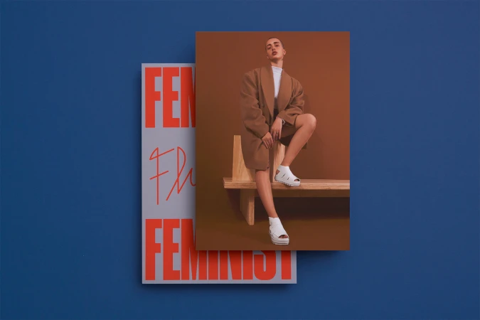 Model wearing a brown coat and white platform shoes seated on a wooden bench with printed promotional materials against a solid blue wall.