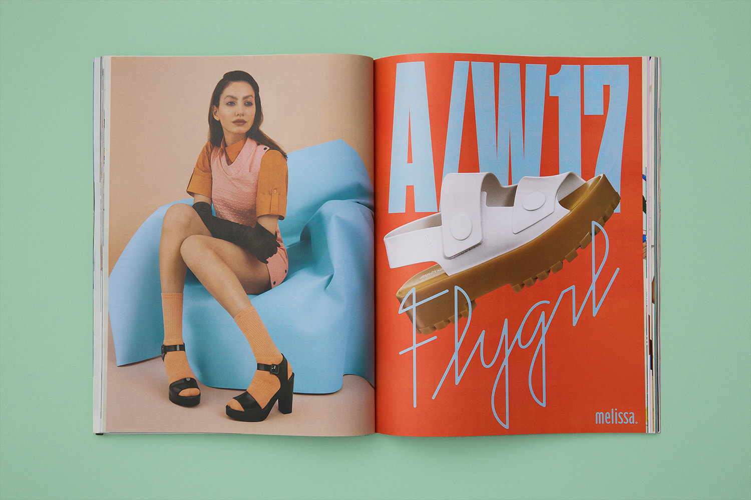 An open magazine spread featuring a woman seated on a blue inflatable chair and a white platform sandal against an orange background.