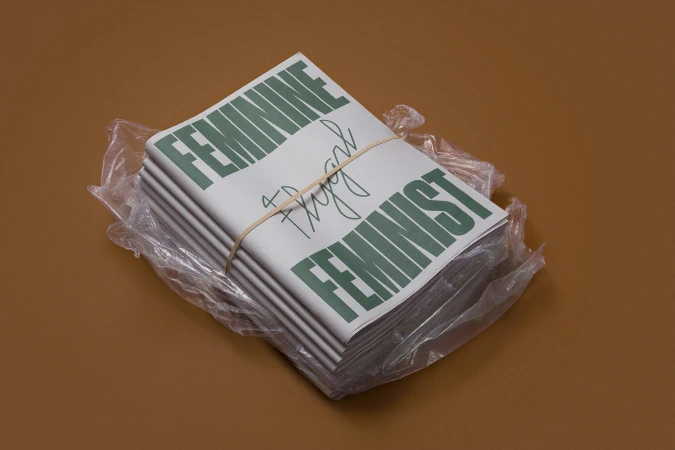 A stack of wrapped printed publications tied with a rubber band resting on a solid brown background.