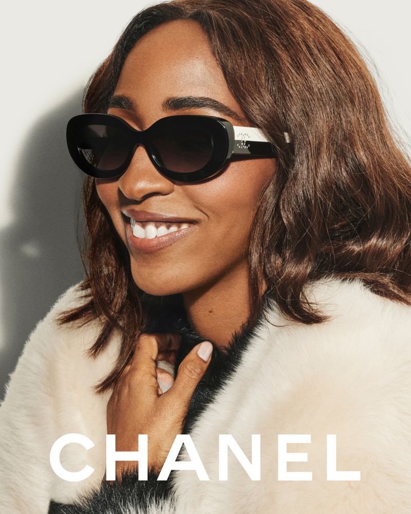 Close-up portrait of Ayo Edebiri wearing black sunglasses and a white textured coat against a plain background