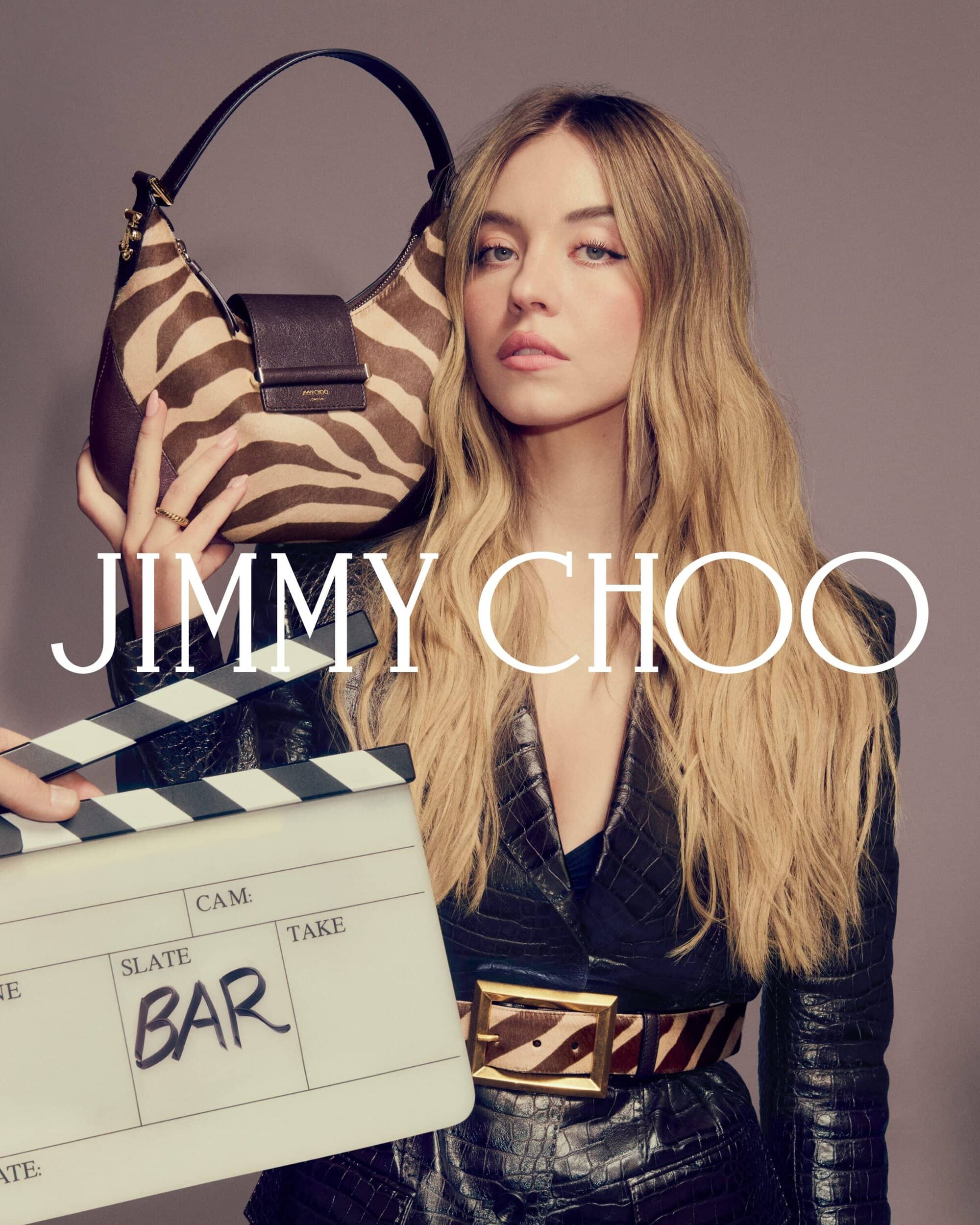 Sydney Sweeney holding a zebra-print handbag and wearing a dark crocodile-embossed blazer for Jimmy Choo Fall 2025 ad campaign.