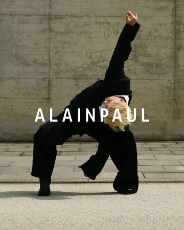 Model in black suit leaning backward against a concrete wall for Alainpaul ad campaign