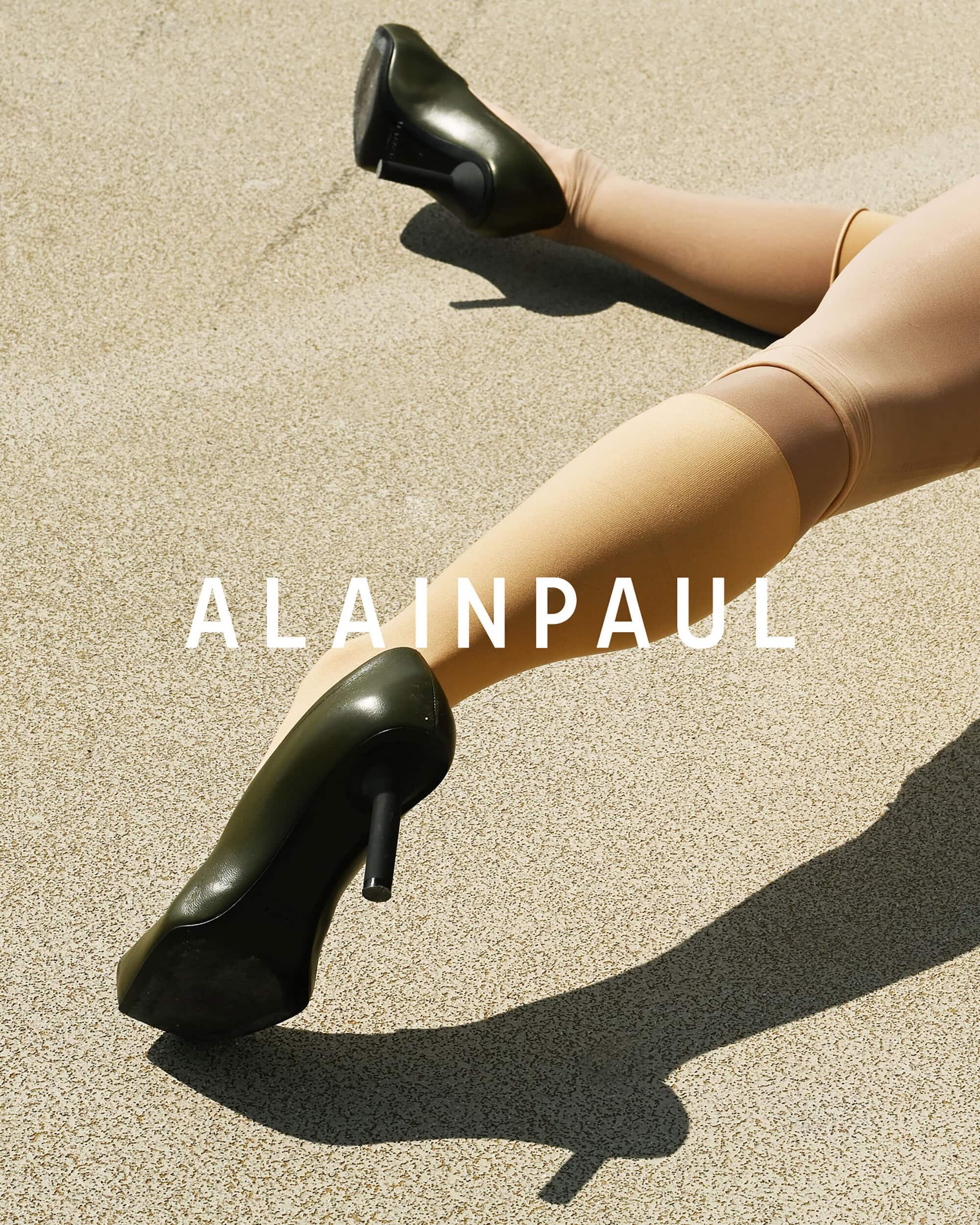 Close-up of legs wearing knee-high stockings and olive green high heels against a textured stone ground.