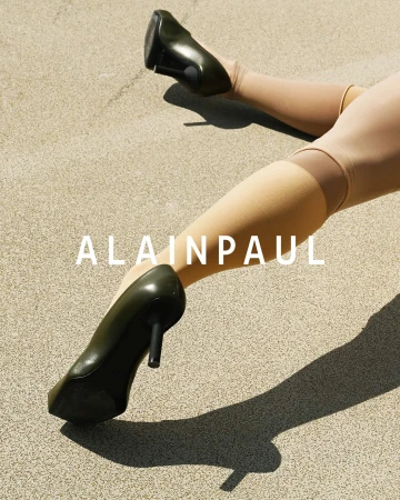Close-up of legs wearing knee-high stockings and olive green high heels against a textured stone ground.