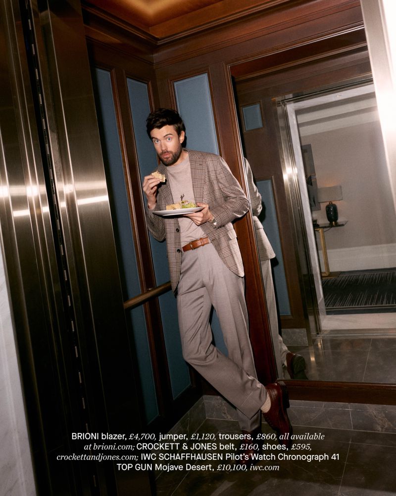 Jack Whitehall in a plaid blazer and trousers eating from a plate inside an elevator, photographed by Stewart Bryden.