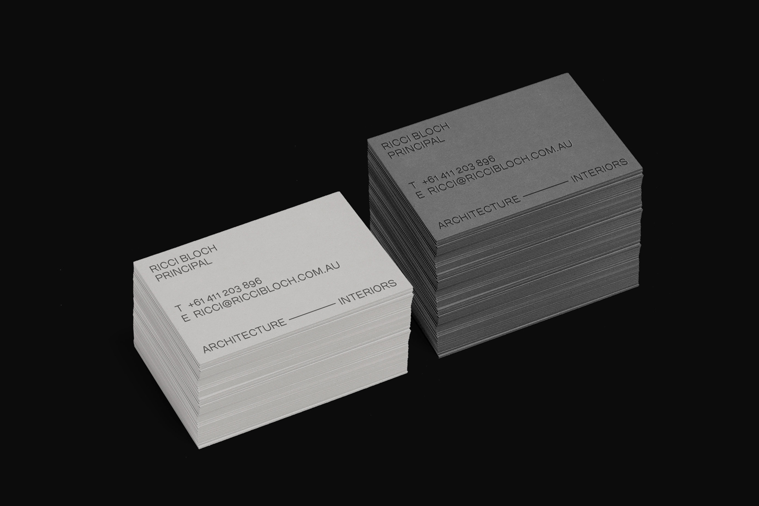 Two stacks of minimalist business cards for Ricci Bloch Architects on a dark background.