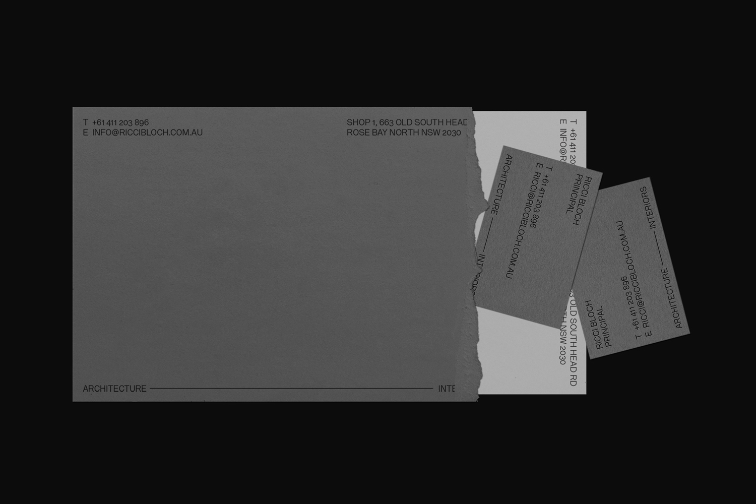 Monochrome brand identity presentation featuring grey stationery items and business cards with minimalist typography against a black background.