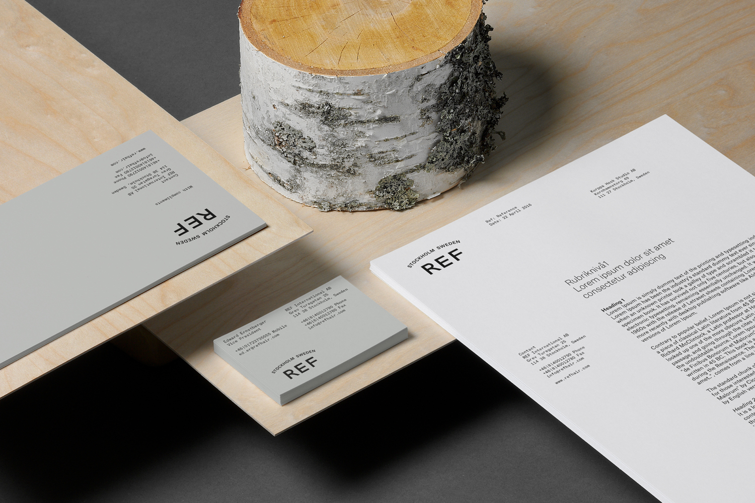 Corporate stationery items including business cards and letterhead featuring REF branding arranged on plywood and wood log sections.