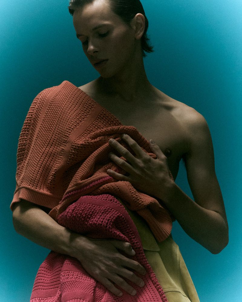 Close-up portrait of a male model holding textured knit garments against a vibrant blue background