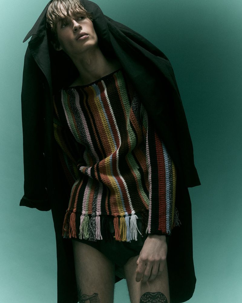 Model wearing striped fringed sweater and dark coat against a gradient teal background for Behind the Blinds project Electric Feel