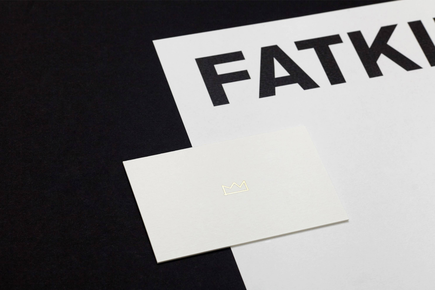 Minimalist brand identity layout featuring a white business card with a gold crown outline placed on a white letterhead and dark surface