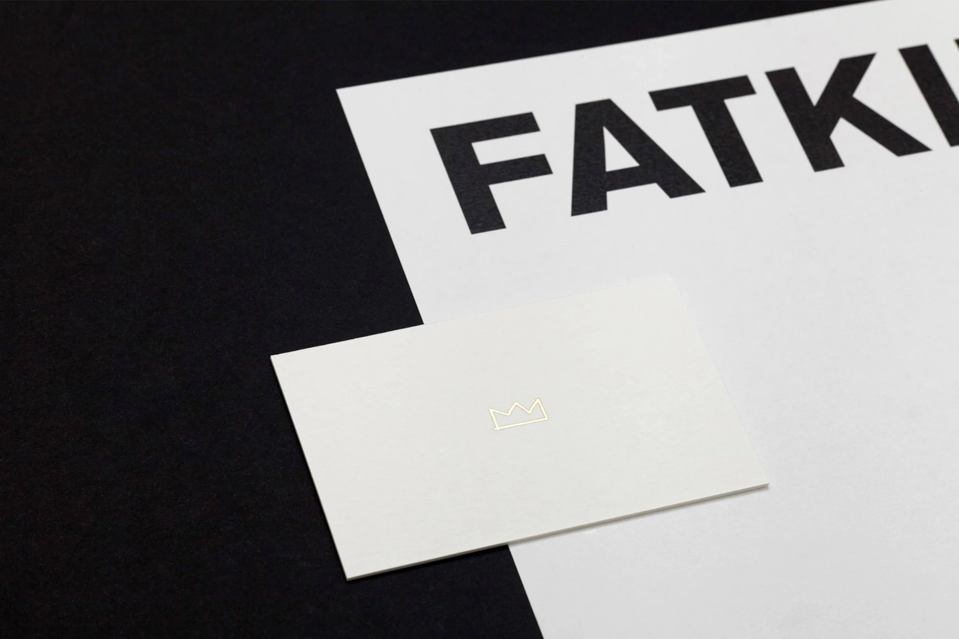 Minimalist brand identity layout featuring a white business card with a gold crown outline placed on a white letterhead and dark surface