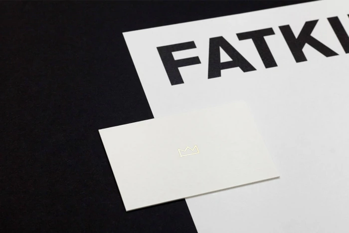 Minimalist brand identity layout featuring a white business card with a gold crown outline placed on a white letterhead and dark surface