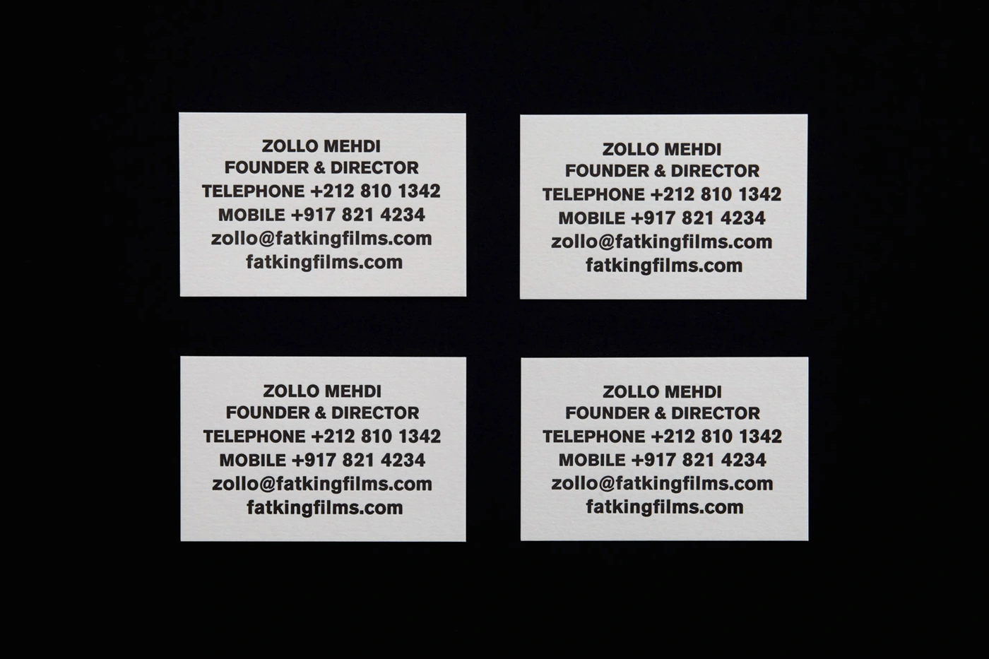Four white business cards arranged in a grid with black typography against a dark background