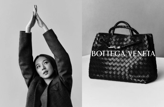 Black and white fashion campaign image featuring a woman in a textured blazer with arms raised beside a woven leather handbag.