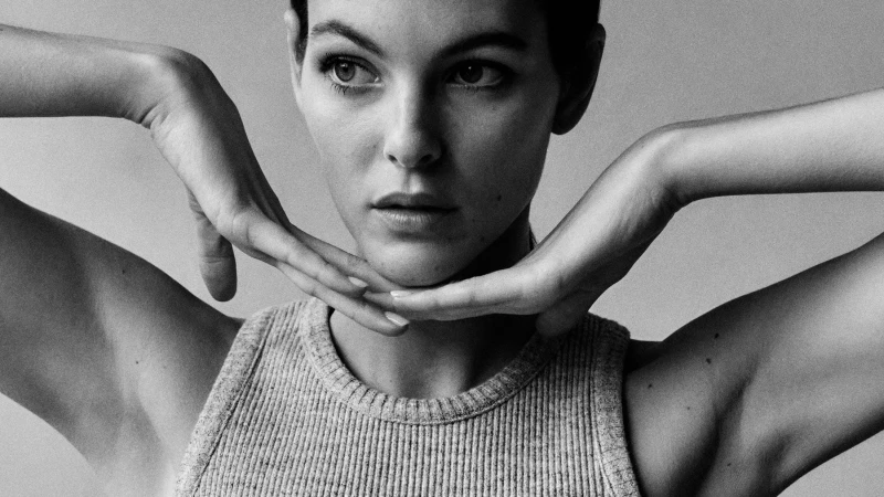 Close-up black and white portrait of a model with short hair resting her chin on her hands, wearing a textured ribbed tank top.