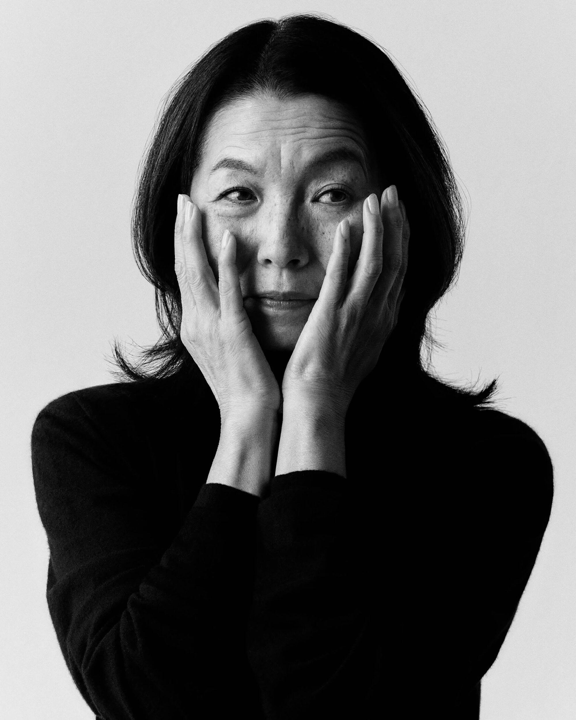 Black and white portrait of a woman holding her face with both hands against a plain light background