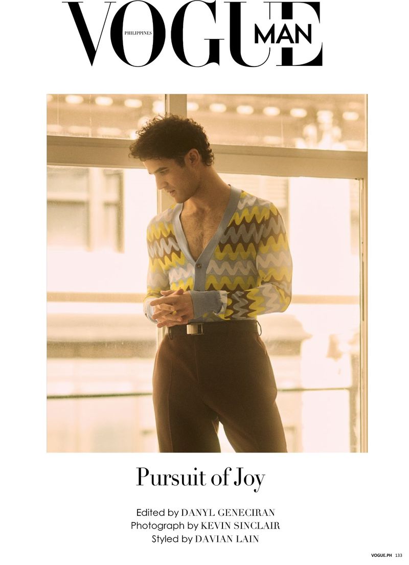 Vogue Man cover featuring a brunette male model in a patterned cardigan and brown pants posing indoors with natural window lighting.