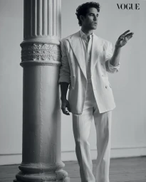 Darren Criss leaning against an ornate neoclassical column wearing a white double-breasted suit for Vogue Philippines editorial