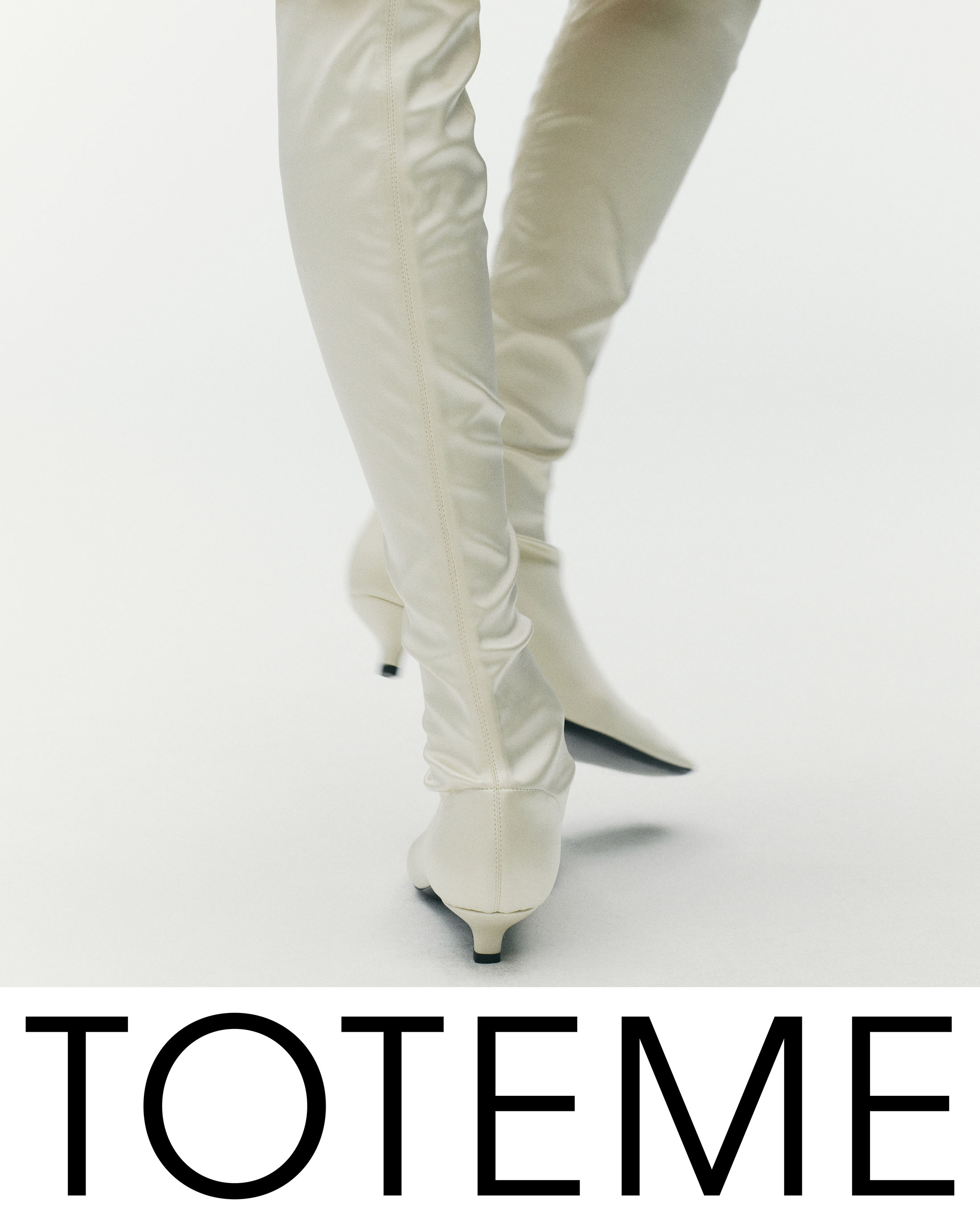 Close-up of a model wearing high white boots against a clean white seamless studio background for Toteme