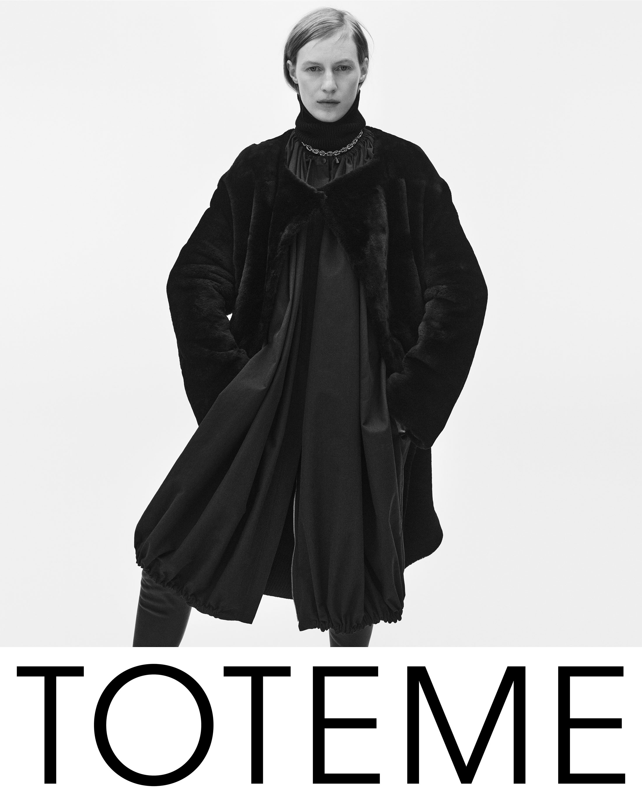 Model Julia Nobis wearing a black coat and turtleneck sweater against a white seamless background for Toteme