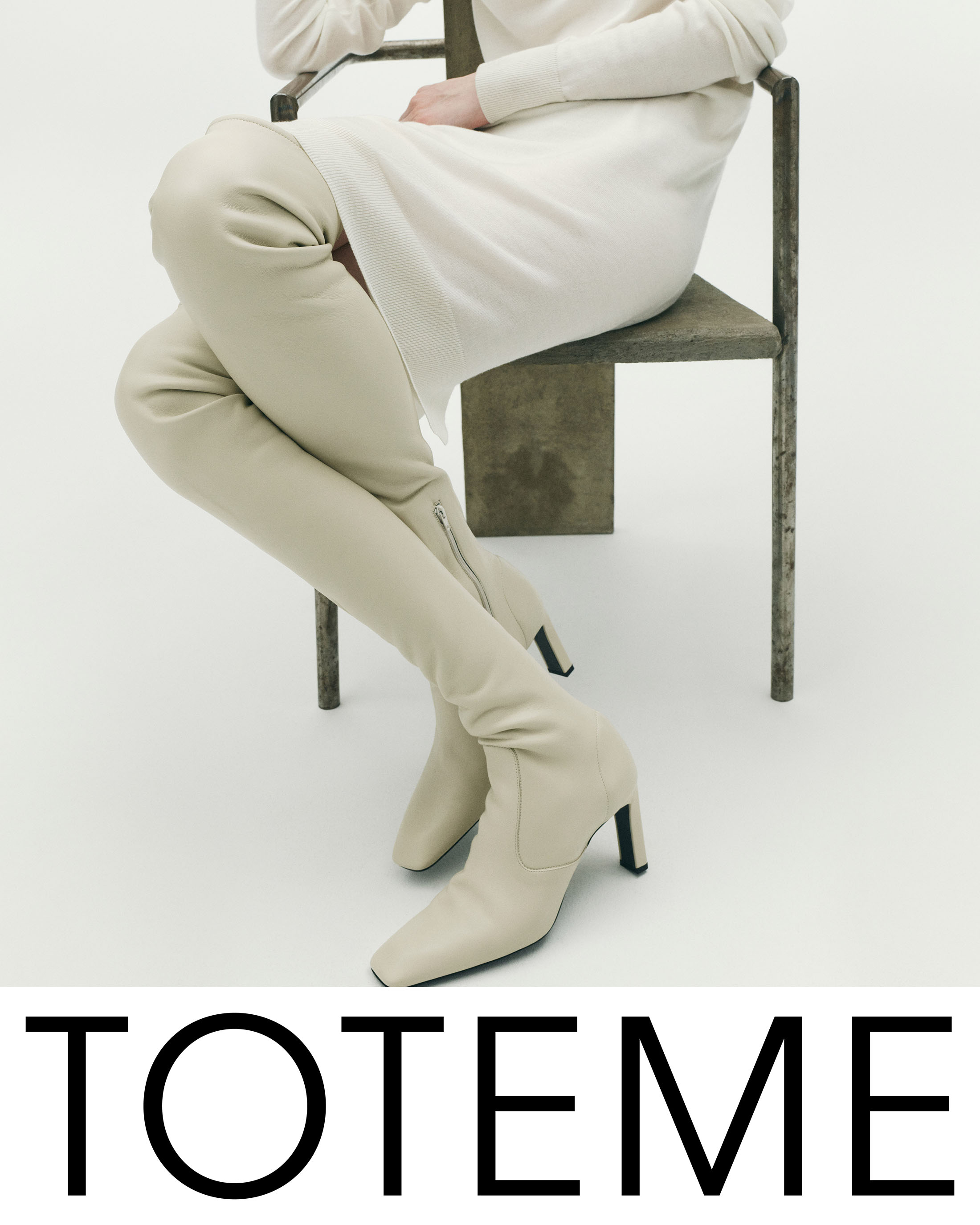 Model seated on a chair wearing an off-white dress and knee-high leather boots against a white background