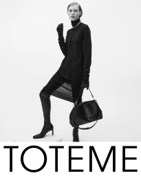 Model in a black turtleneck dress and high boots holding a black leather handbag against a plain white background