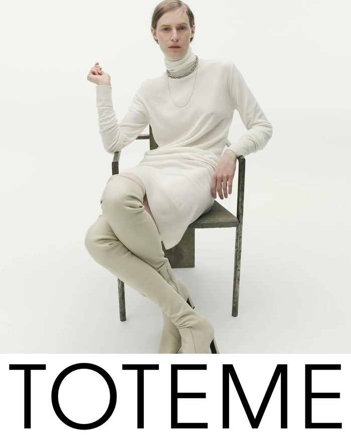 Model Julia Nobis seated in an armchair wearing a cream turtleneck dress and knee-high boots for Toteme Fall 2025 campaign.