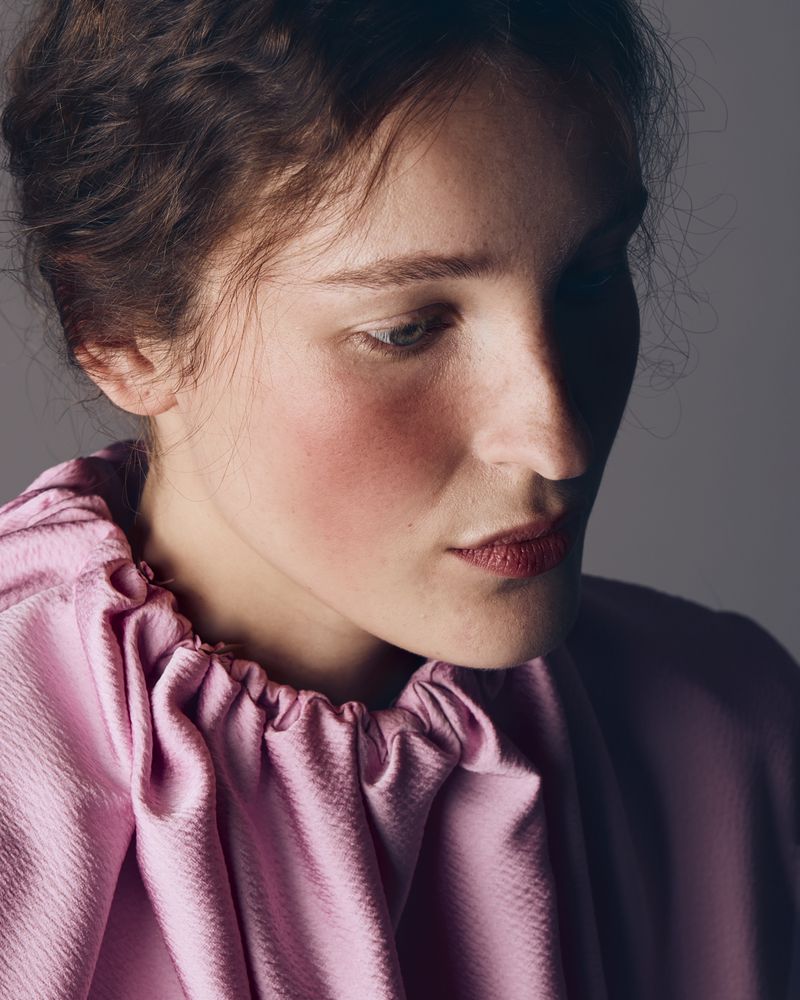 Portrait of a woman wearing a pink ruffled high neck top against a neutral grey studio background