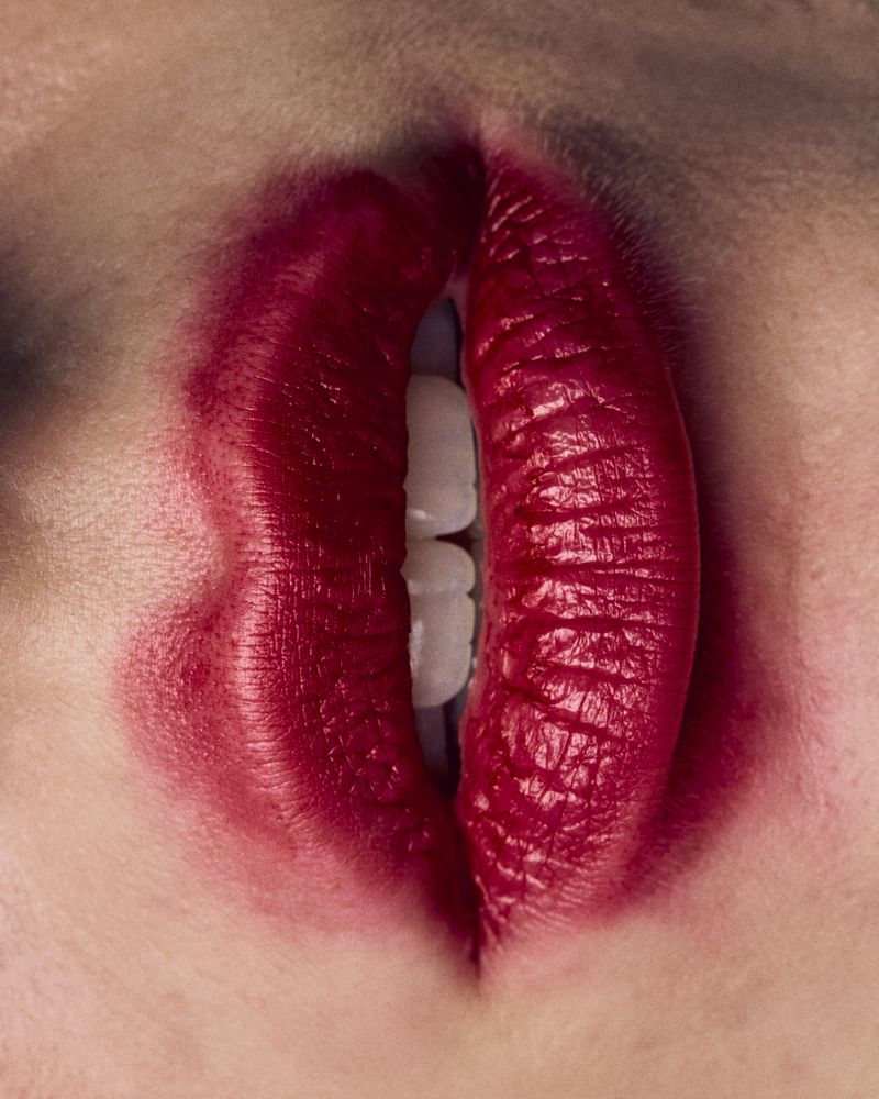 Extreme close-up macro view of lips wearing deep red lipstick with visible teeth