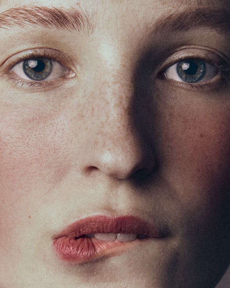 Close-up portrait of a woman biting her lip with detailed skin texture and freckles for Vogue Portugal