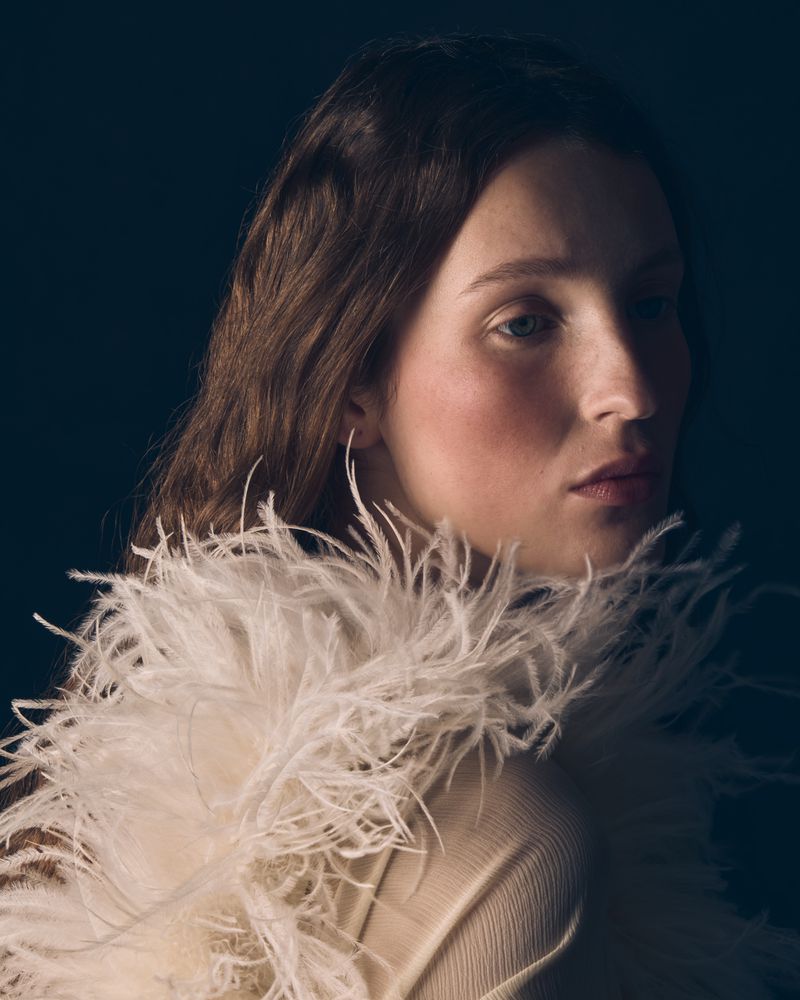 Portrait of a woman wearing a white feather collar against a dark background for Vogue Portugal