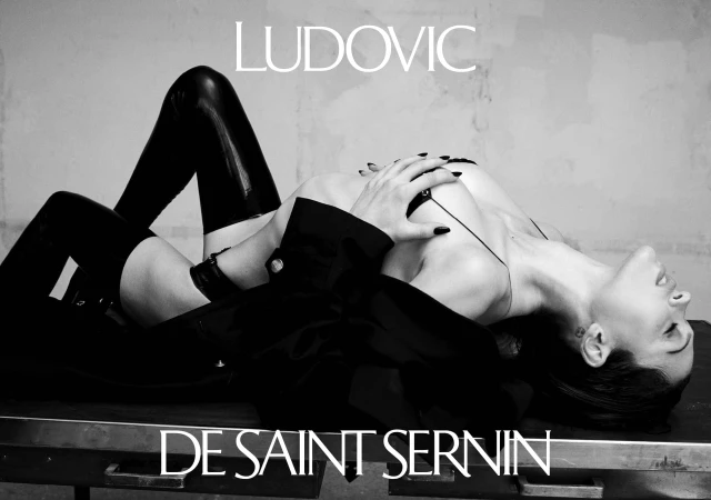 Model lying on a metallic surface wearing dark thigh-high boots and a jacket in a black and white fashion campaign photograph