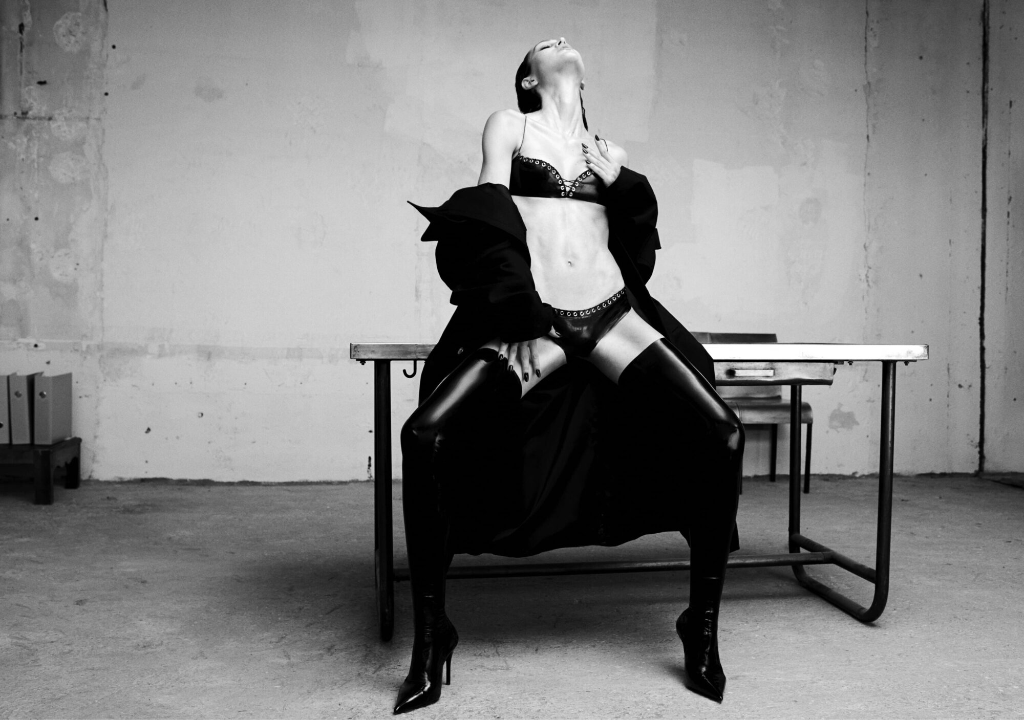 Model Amelia Gray posing on a table wearing black lingerie and thigh-high boots for Ludovic de Saint Sernin.
