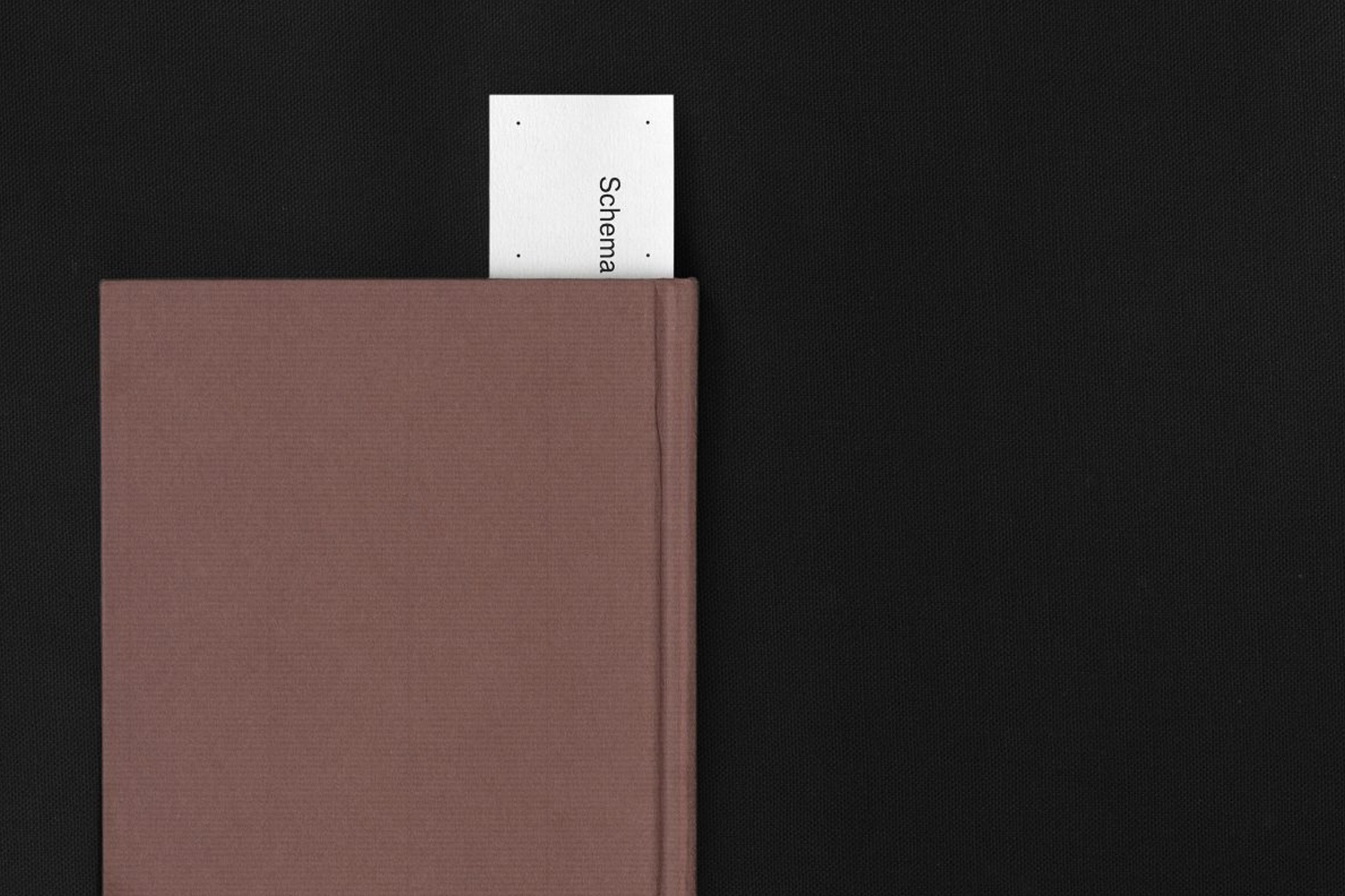 Brown cloth-bound book with a small white business card bookmark inserted at the top against a black background.