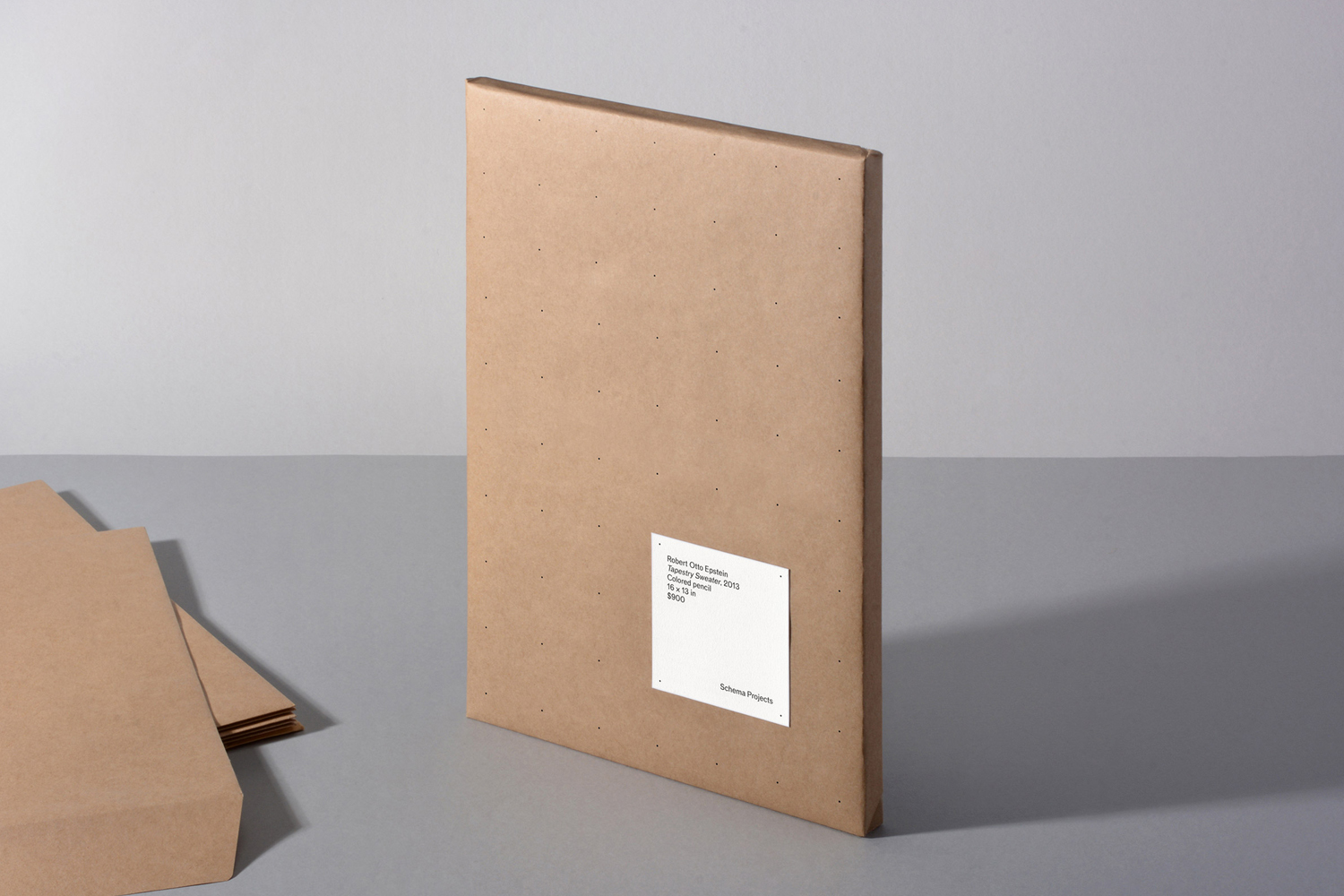 Brown paper portfolio folder standing on a grey surface with a white label for Schema Projects brand identity.