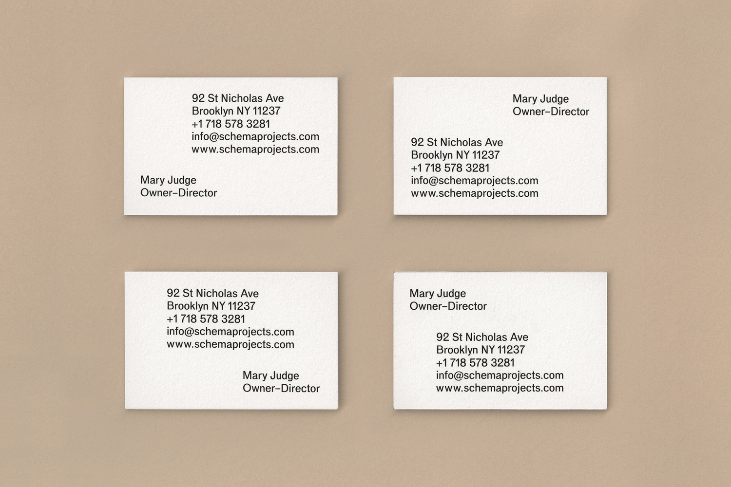 Four white business cards with black typography arranged in a grid on a light beige textured surface.
