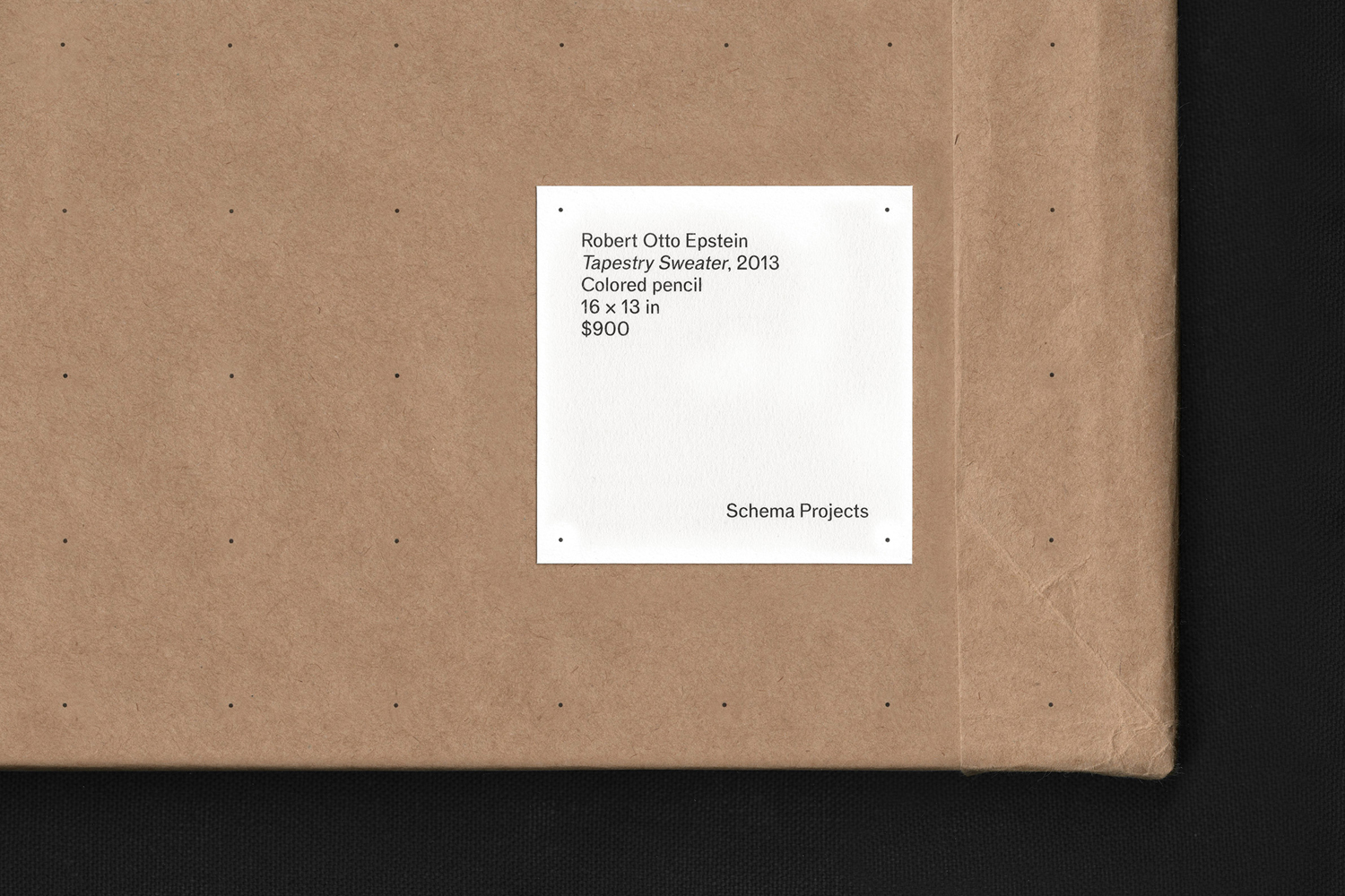 A white square art label affixed to a brown paper envelope with black grid dots against a dark textured background.