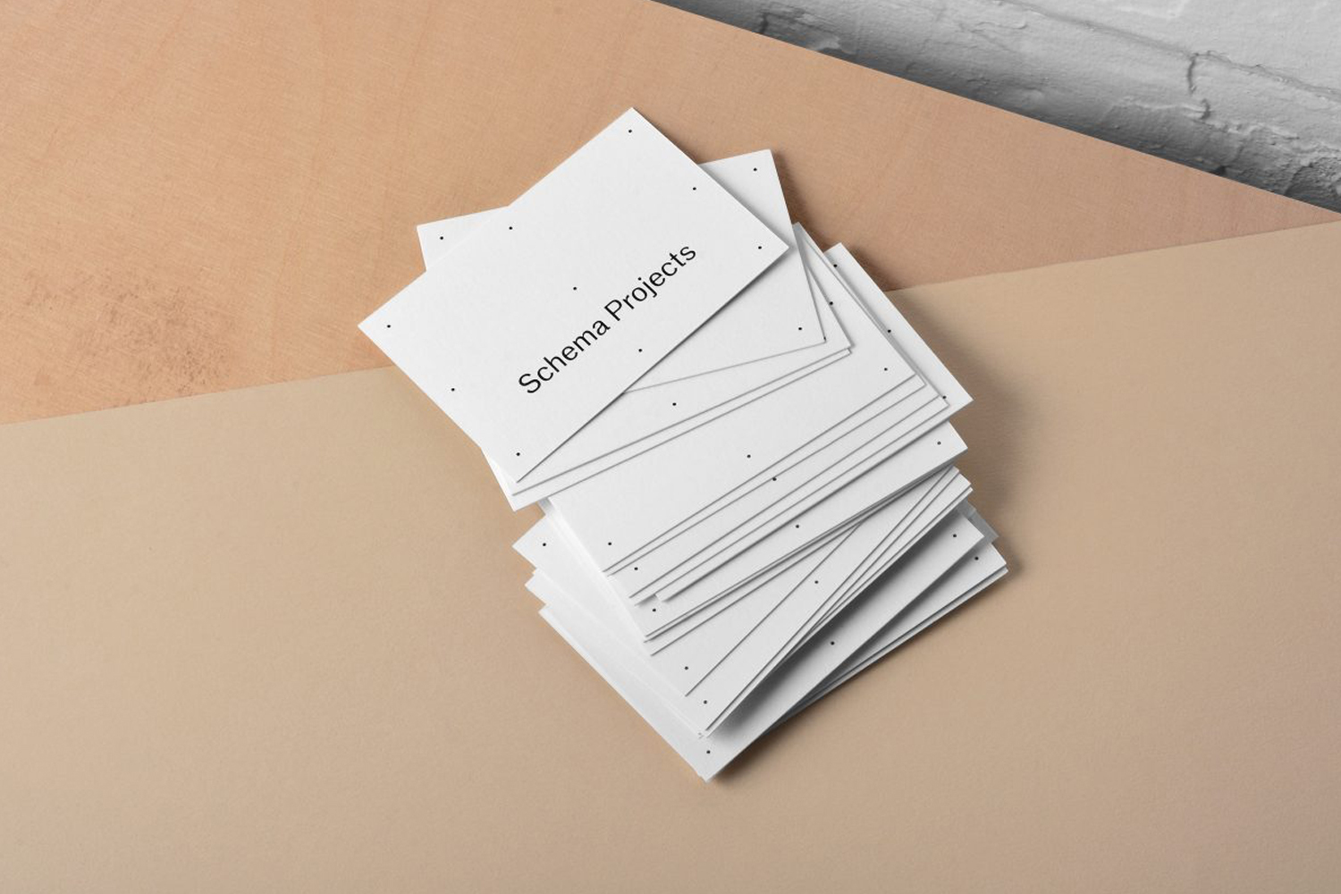 Stack of white business cards with small black dots and the text Schema Projects resting on a beige and brown surface.