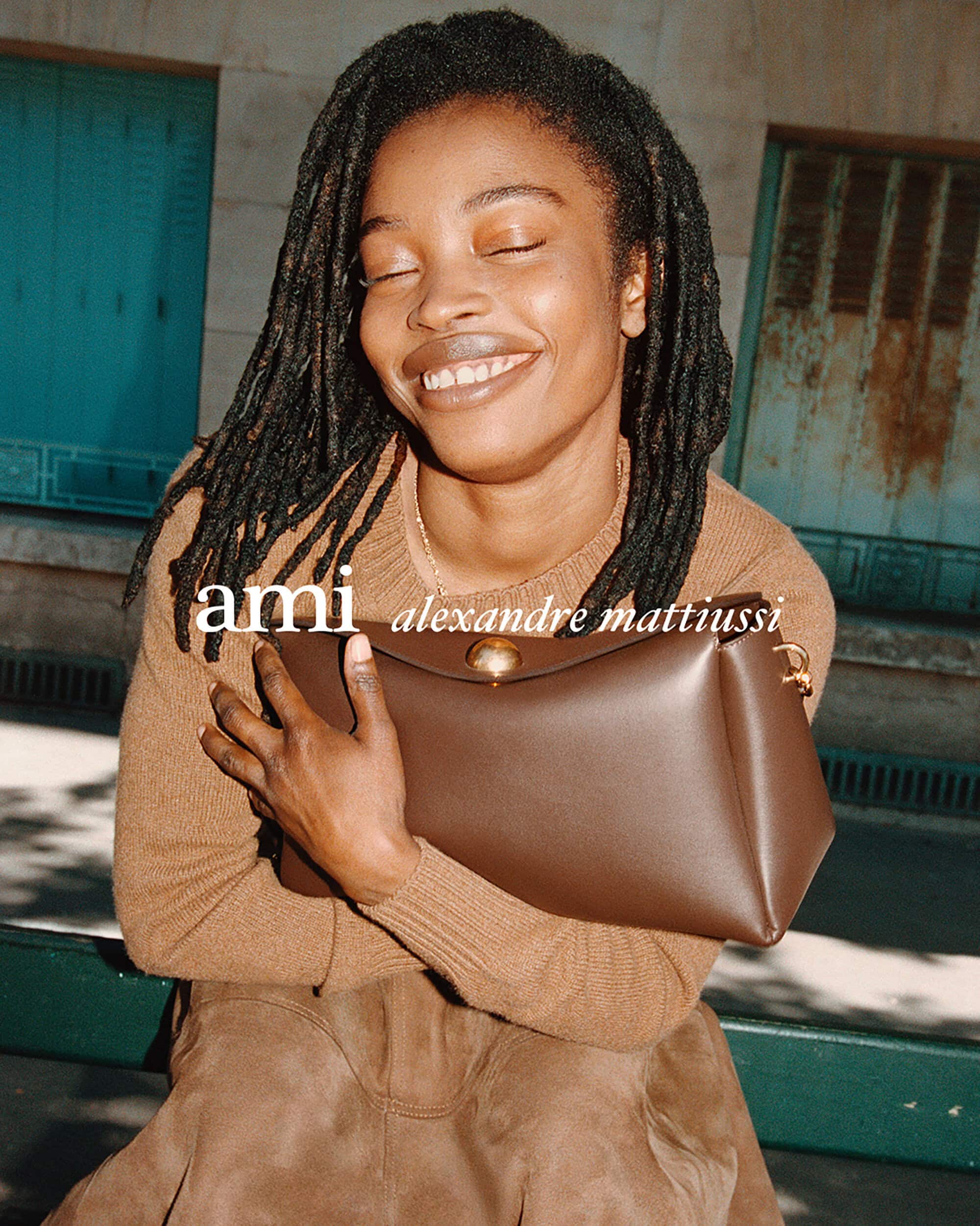 Smiling Black woman holding a brown leather handbag outdoors against an urban architectural building backdrop