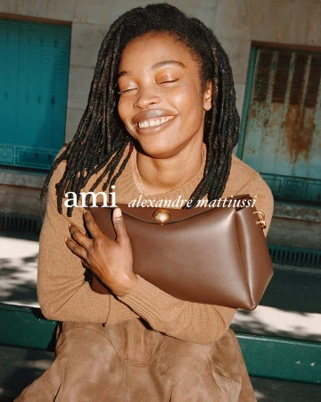 Smiling Black woman holding a brown leather handbag outdoors against an urban architectural building backdrop