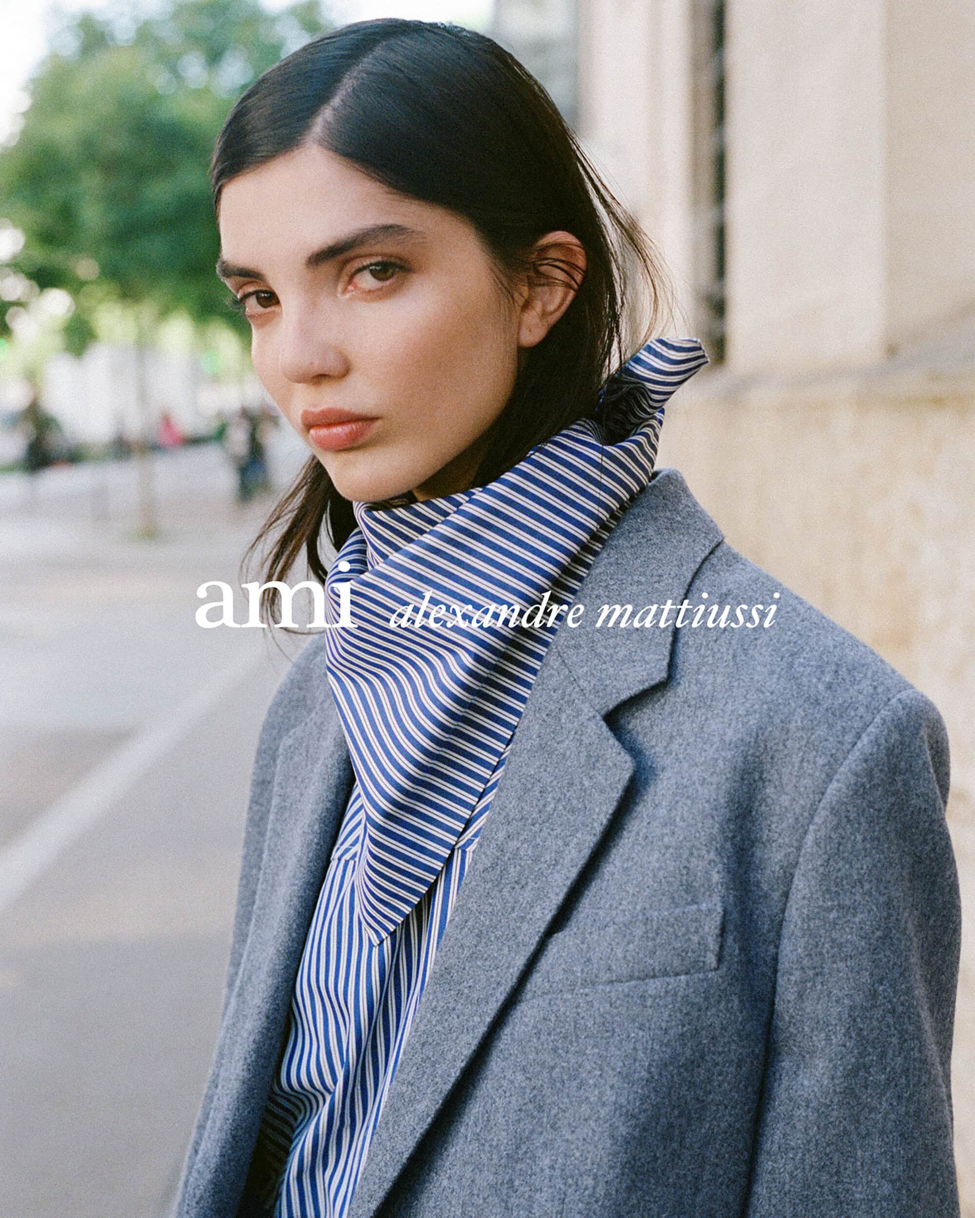 Close-up portrait of a woman wearing a grey wool blazer and a blue striped silk scarf outdoors.